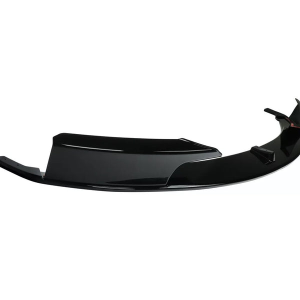 A glossy black car bumper lip rests against a white background, showcasing its aerodynamic design with sharp edges and smooth curves.