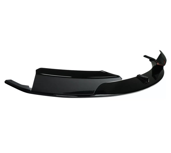 A glossy black car bumper lip rests against a white background, showcasing its aerodynamic design with sharp edges and smooth curves.
