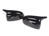 Two glossy black car side mirror covers lie on a blank white surface, each with a sleek, aerodynamic design featuring smooth, curved lines.