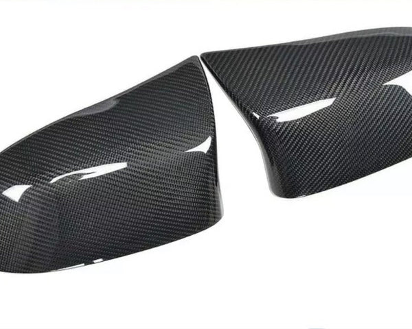 Two glossy carbon fiber car mirror covers rest on a white surface, reflecting light and showcasing their textured pattern.