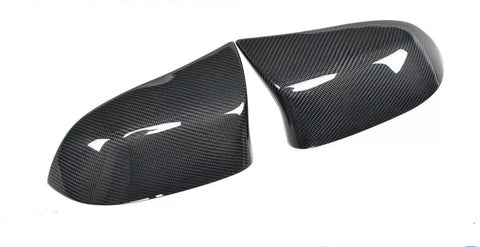 Two glossy carbon fiber car mirror covers rest on a white surface, reflecting light and showcasing their textured pattern.