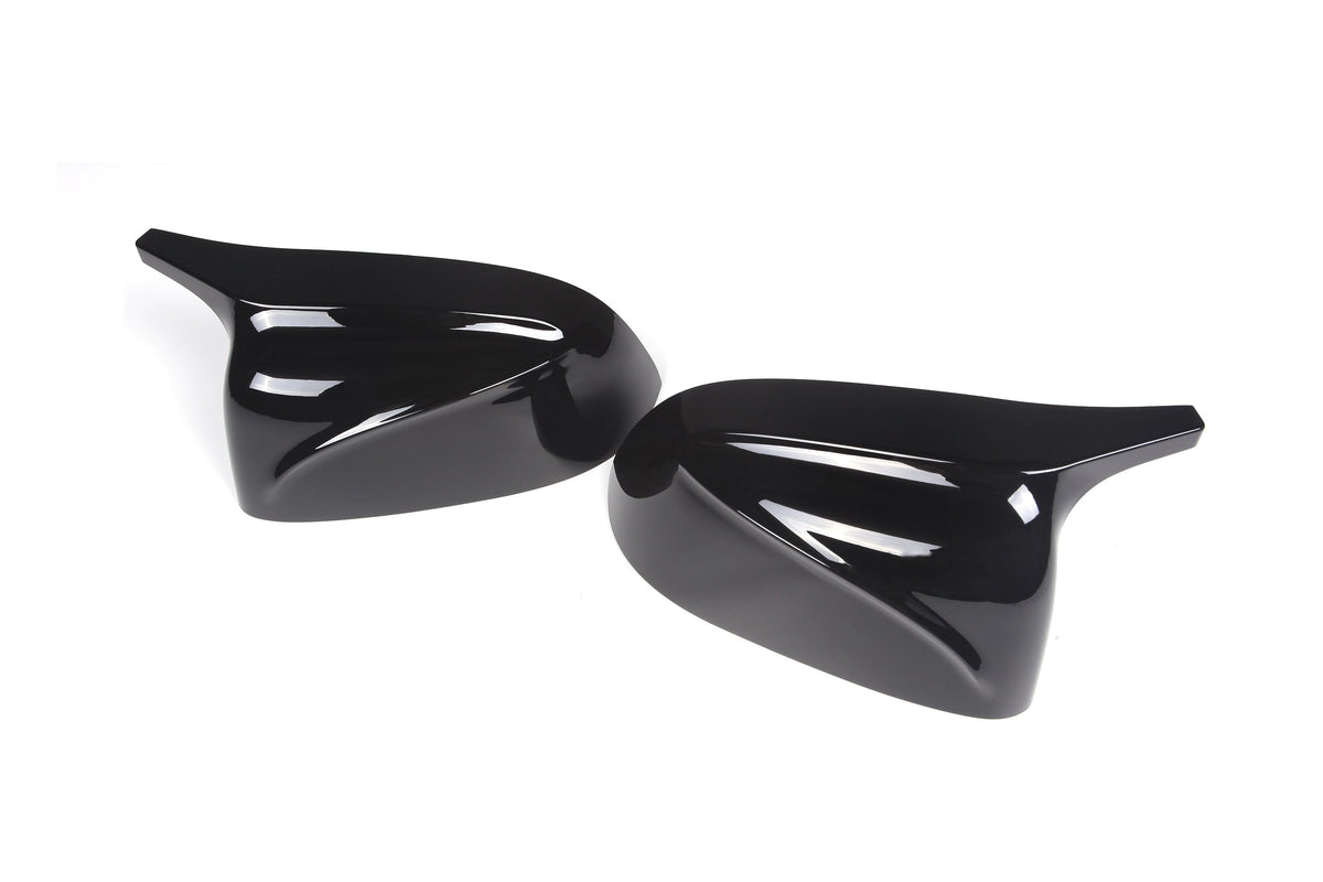 Two glossy black side mirror covers reflect light, positioned on a white background. The covers have a sleek, aerodynamic design, suggesting use for a vehicle.