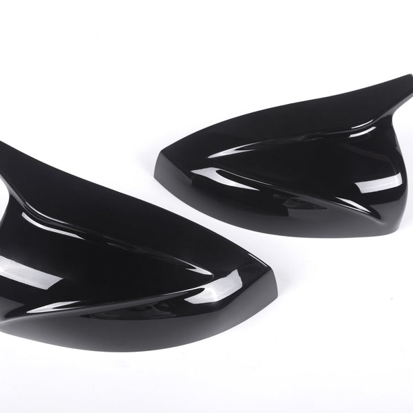 Two sleek, black, aerodynamic car mirror covers lay side by side on a plain white background, emphasizing their glossy finish and curved design.