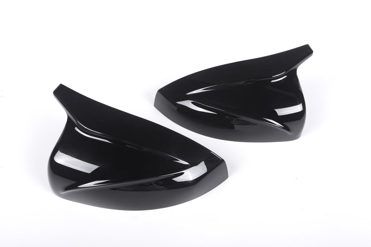 Two sleek, black, aerodynamic car mirror covers lay side by side on a plain white background, emphasizing their glossy finish and curved design.