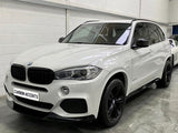 A white BMW SUV is parked indoors on a concrete floor, featuring black wheels and a front license plate that reads 