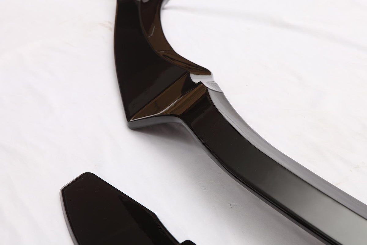 A glossy black automotive trim piece lies on a white surface, featuring smooth, angular shapes and reflective curves, suggesting a component for vehicle customization or aesthetics.