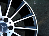 Wheel rim with a metallic Mercedes-Benz logo and black spokes, resting still, set against a textured asphalt surface.