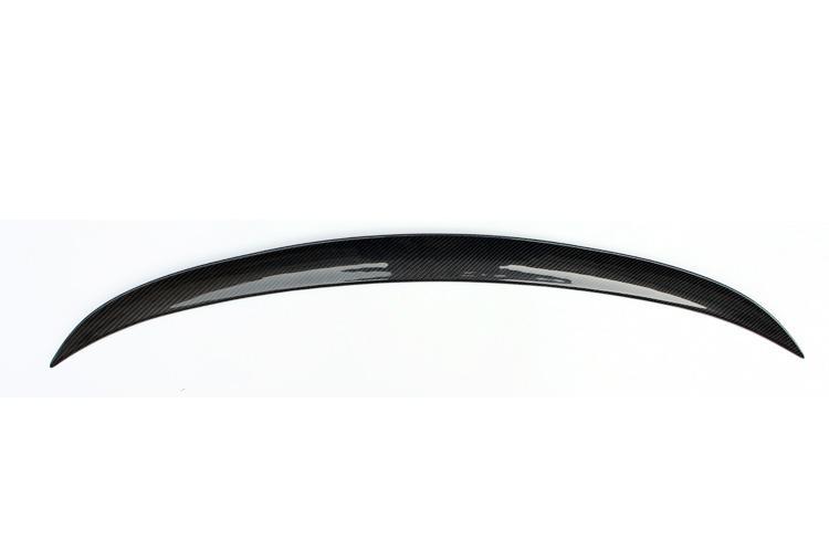 A glossy, black carbon fiber car spoiler arcs gracefully, displayed against a plain white background, highlighting its sleek and aerodynamic design.