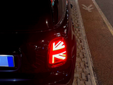 A car with illuminated Union Jack taillight is parked on a cobblestone road. It is positioned next to a bike lane symbol in a nighttime urban environment.