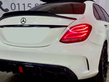 A white Mercedes-Benz car is parked inside a garage, showcasing its illuminated rear lights. The background displays a wall with phone numbers beginning with 