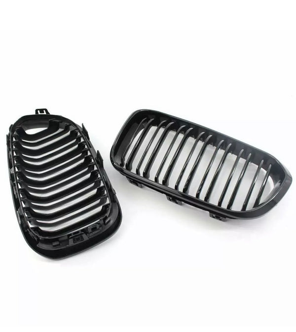 Two black car grille parts, each with parallel vertical slats, are positioned side by side. They are set against a plain, white background.