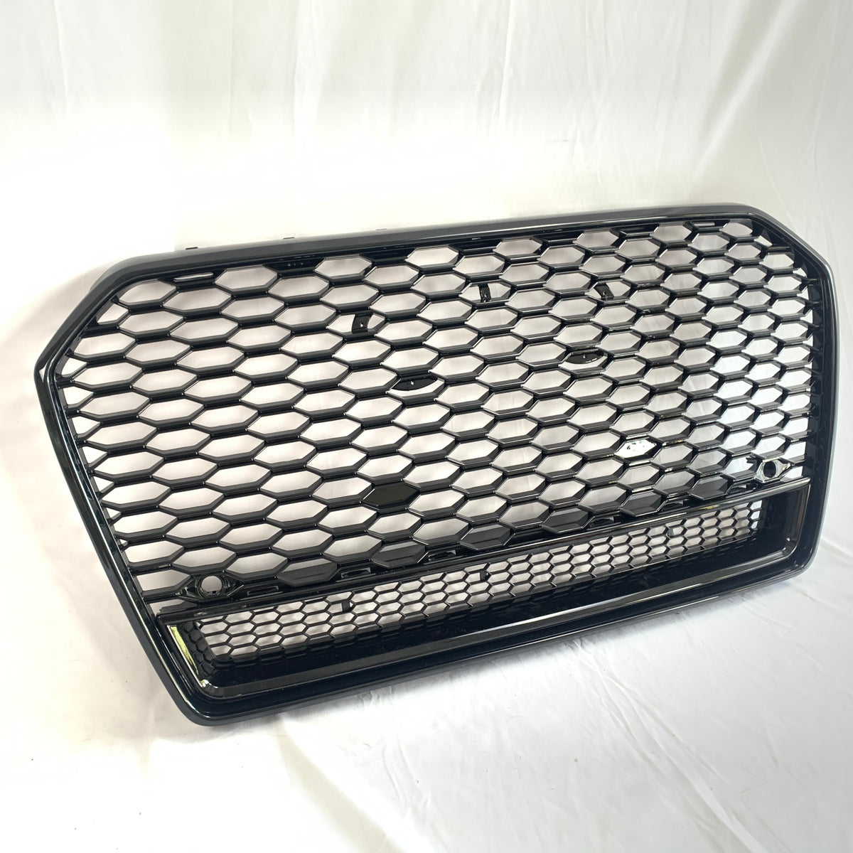 A black hexagonal mesh car grille rests against a white background. The grille features a honeycomb pattern and two round mounting points, suggesting automotive use.