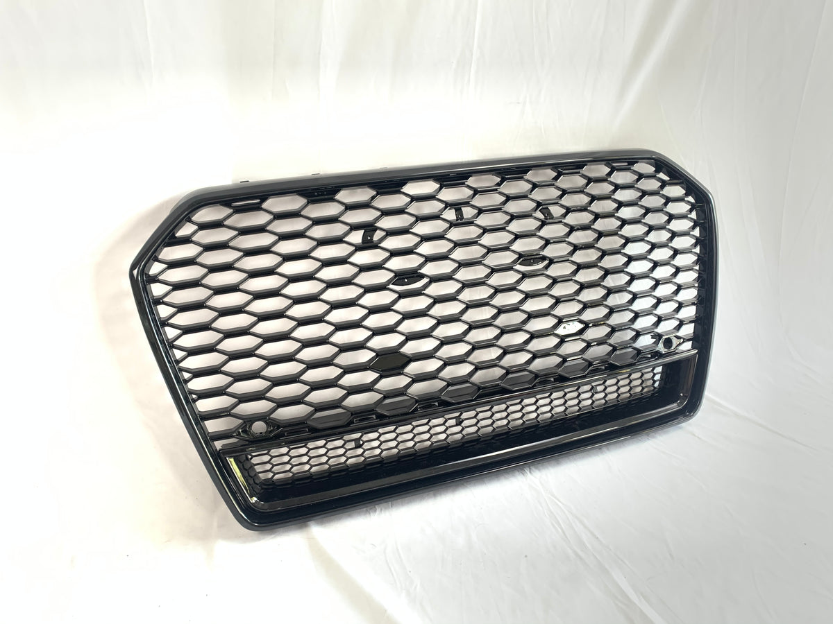 A black hexagonal mesh car grille rests against a white background. The grille features a honeycomb pattern and two round mounting points, suggesting automotive use.
