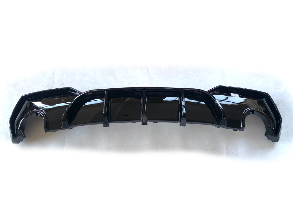 A glossy black car bumper with curved edges and slots rests on a plain white surface, reflecting light from its smooth surface.