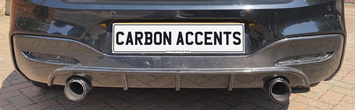 Car rear end with dual exhaust pipes, carbon fiber diffuser, and a license plate reading "CARBON ACCENTS." It’s parked on a brick driveway.