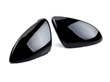 Two shiny black car mirror covers are lying side by side on a plain white background, reflecting light softly across their smooth, contoured surfaces.