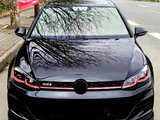 A shiny black car with red accents is parked on a tree-lined street. The windshield displays the letters 