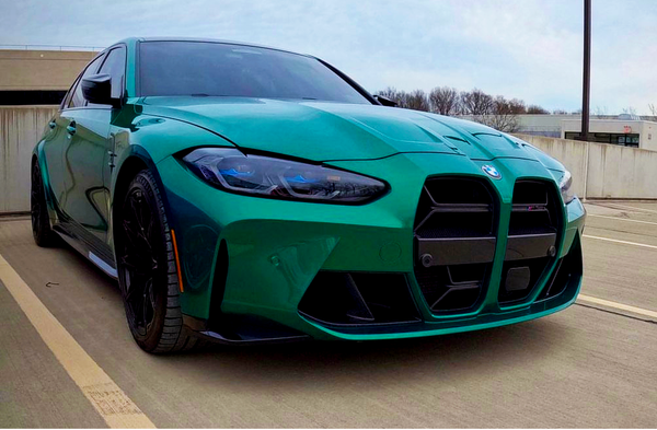 A green sports car parked in an empty rooftop lot under an overcast sky, featuring a prominent grille and sleek design, with trees and buildings in the background.