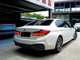 A white BMW sedan is parked outside a building with a sign in Chinese characters. Several other vehicles are nearby in a parking area, including a gray SUV.