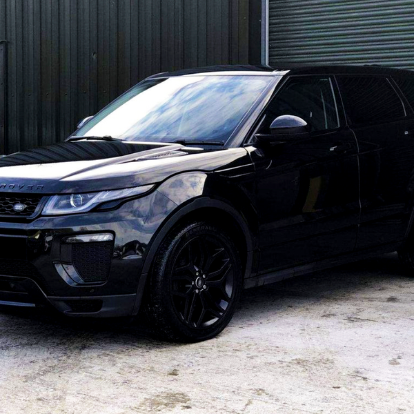 A black Range Rover parked on a concrete surface beside a dark corrugated metal building with a closed door labeled "3."