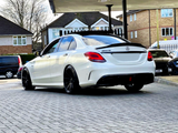 A white Mercedes-AMG C43 with black rims is parked under a canopy, surrounded by residential buildings.