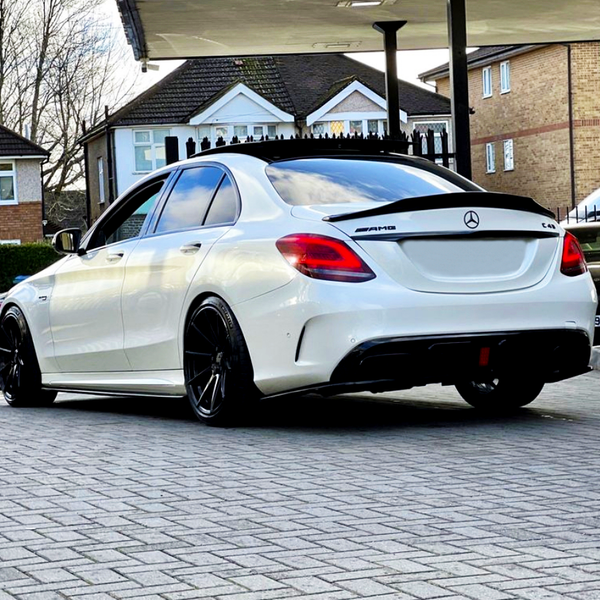 A white Mercedes-AMG C43 with black rims is parked under a canopy, surrounded by residential buildings.