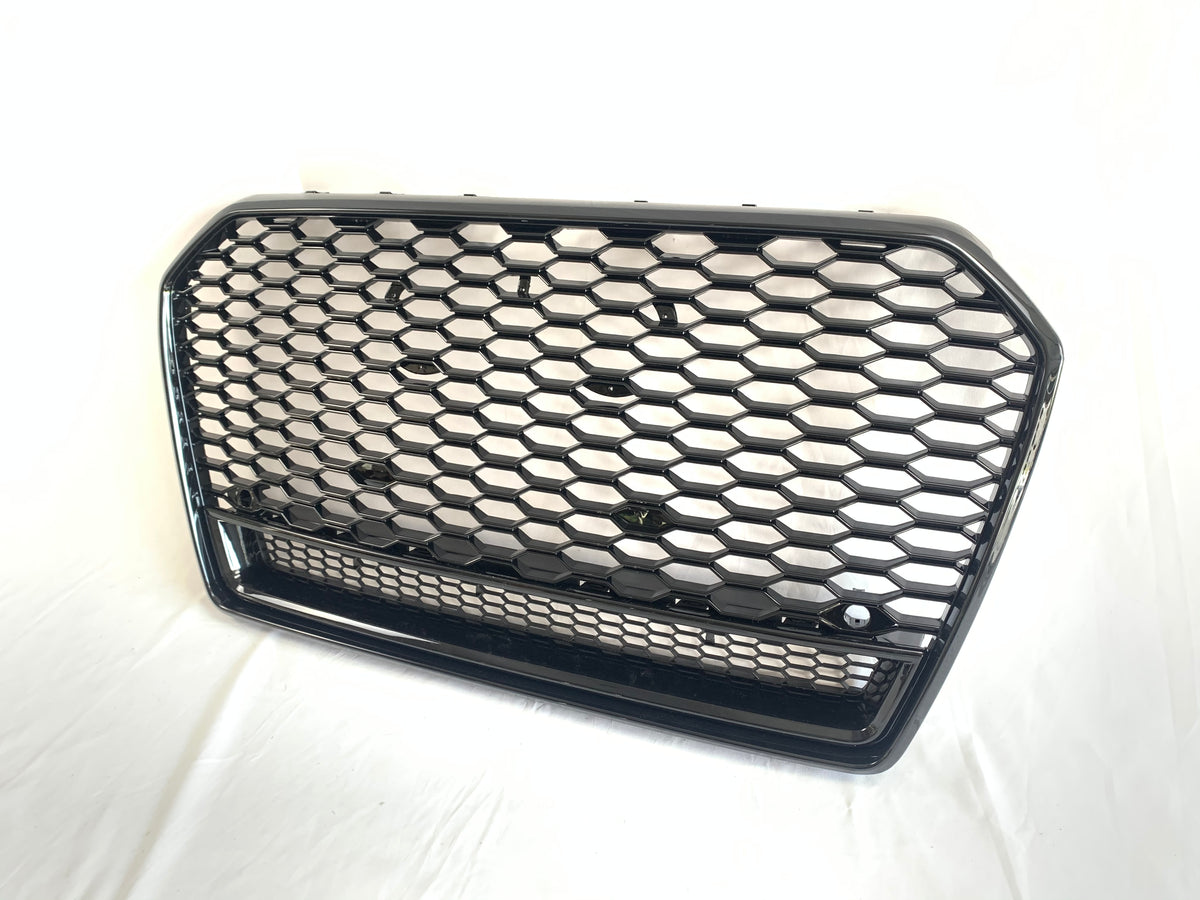 A hexagonal-patterned car grille, featuring a glossy black finish, rests on a white surface. The grille's design includes a prominent honeycomb structure, commonly used for automotive front ends.