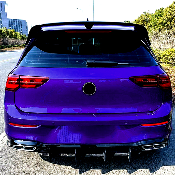 Purple car parked on a road; rear view shows taillights, dual exhausts, and a rear wiper. Surroundings include a building and greenery under clear skies.