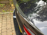 A car with a carbon fiber spoiler reflects foliage above, showing badge 