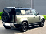 A green SUV is parked on a paved area with a spare tire mounted on its rear. It’s adjacent to a grassy lawn and a gray wall.