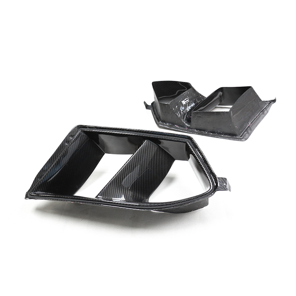 Two carbon fiber car parts are positioned separately on a plain white background, showcasing their sleek, angular shapes and glossy surfaces.