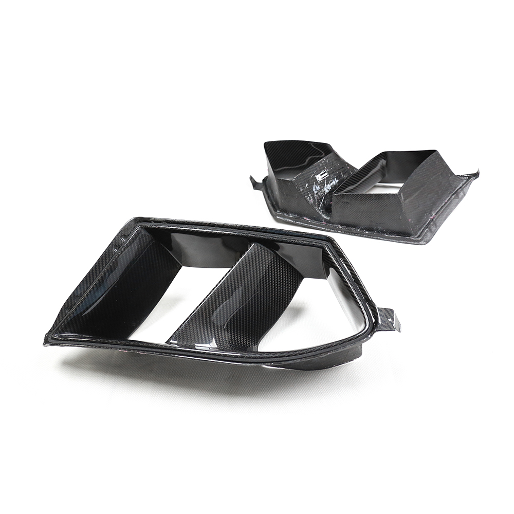 Two carbon fiber car parts are positioned separately on a plain white background, showcasing their sleek, angular shapes and glossy surfaces.