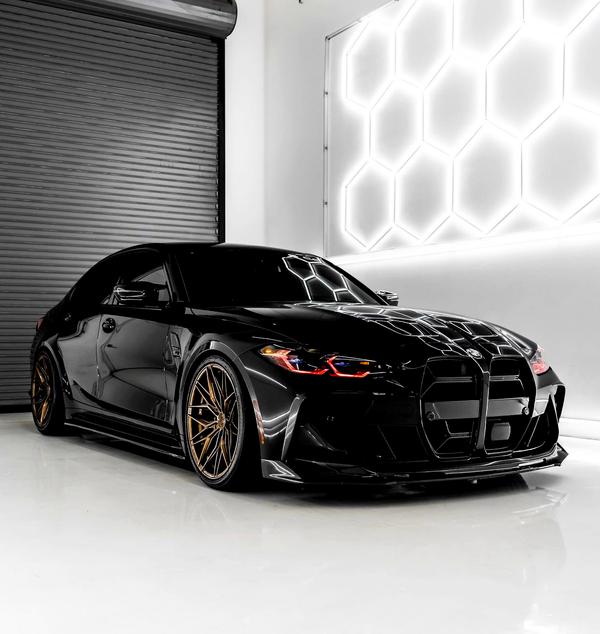 A sleek black sports car with bronze wheels is parked in a modern garage, reflecting hexagonal white lights from the wall, contrasting with a dark roller door.