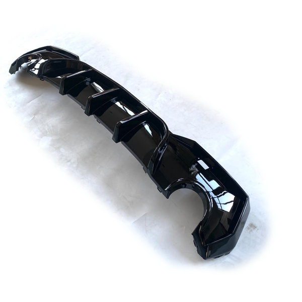 A glossy black car component, likely a diffuser, lies on a plain white surface. It features multiple aerodynamic fins and curves strategically positioned along its length.