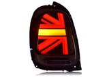 A car taillight illuminated in a Union Jack pattern emits red and yellow light within a black casing against a white backdrop.