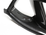 Carbon fiber auto part with a sleek, glossy finish, showing intricate patterning. The part is viewed close-up in a neutral setting, emphasizing its texture and craftsmanship.