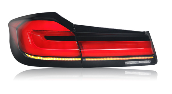A sleek taillight, glowing red, features horizontal light bars and an amber strip along the bottom, set against a reflective white background. No text present.