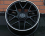 A black alloy wheel with a silver trim featuring a Mercedes-Benz logo rests against a brick wall. The AMG insignia is visible on the top part of the rim.