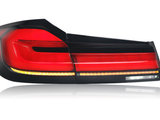 A car taillight, illuminated in red and amber, reflects on a white surface. The sleek design features multiple segments, with a glossy black frame accentuating its modern appearance.