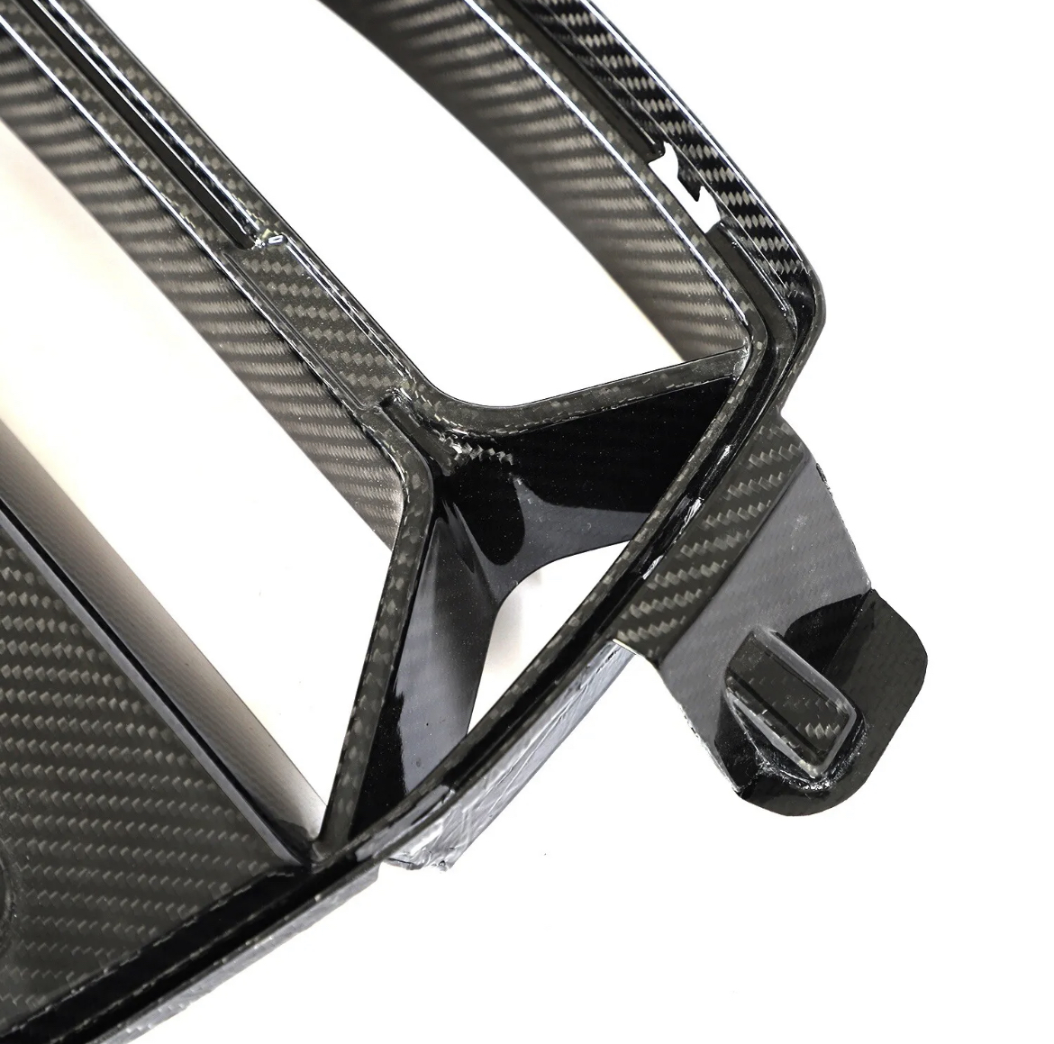 Carbon fiber car part, featuring a sleek, angular design with precise edges, lies on a smooth surface, highlighting its glossy, patterned finish and craftsmanship.
