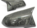 Two glossy, dark carbon fiber car mirror covers resting on a plain white background, highlighting their sleek design and textured surface reflecting light.