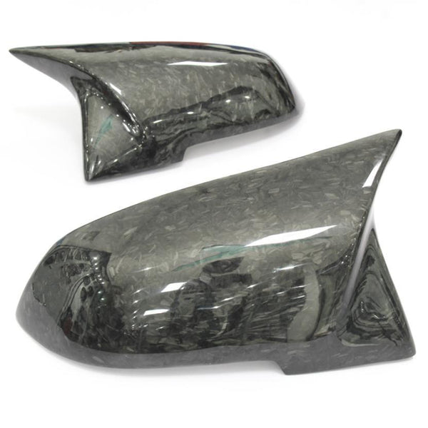 Two glossy, carbon fiber car mirror covers rest on a white surface, showcasing their reflective texture and sleek, aerodynamic design.