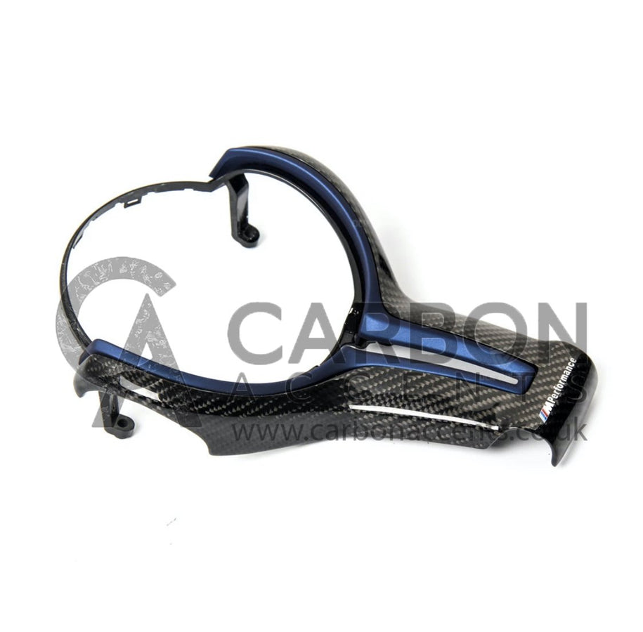 A carbon fiber car steering wheel trim with a blue accent rests on a plain surface. Text reads "M Performance" and a watermark "CARBON ACCENTS www.carbonaccents.co.uk" overlays the image.