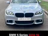 A silver BMW 5 Series (2010-16) with gloss black double slat grills is parked on a street, surrounded by grass. The front plate reads 