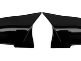 Two glossy black car mirror covers lay side by side on a white background, facing each other symmetrically. They are smooth and have a sleek, aerodynamic design.