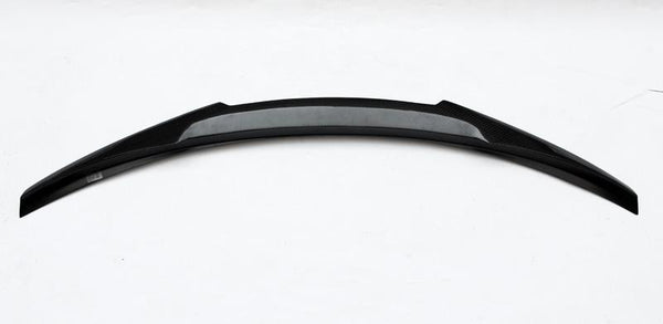 A curved black car spoiler, with a carbon fiber texture in the center, lies on a plain white background.