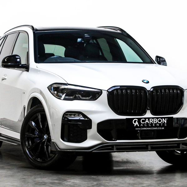 A white SUV with black accents is parked on a polished concrete floor in a studio setting. The front license plate reads, "CARBON ACCENTS www.CARBONACCENTS.CO.UK."