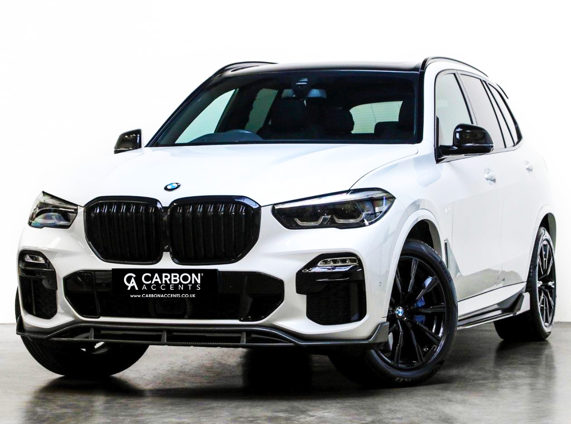 White SUV with black grille is parked, viewed from the front. License plate reads "CARBON ACCENTS www.carbonaccents.co.uk." The background is a plain, light-colored space.