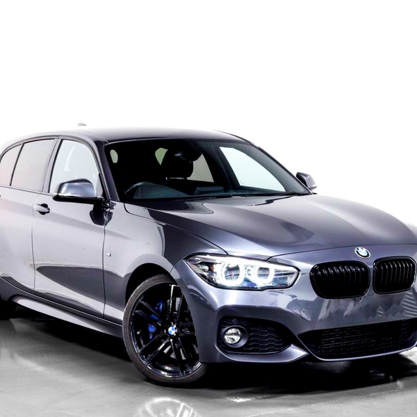 A gray BMW hatchback, featuring sleek black alloy wheels and prominent headlights, is parked on a reflective gray floor against a white background.