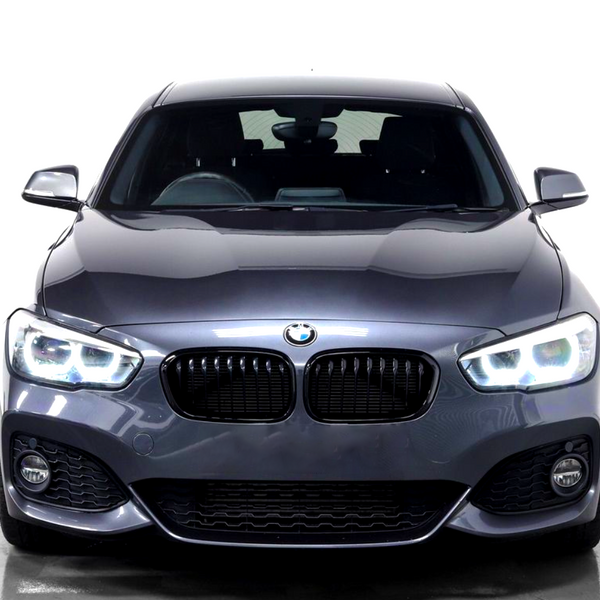 A gray BMW car, featuring illuminated headlights, is stationary in a bright, plain white environment, highlighting its sleek design and curved contours.